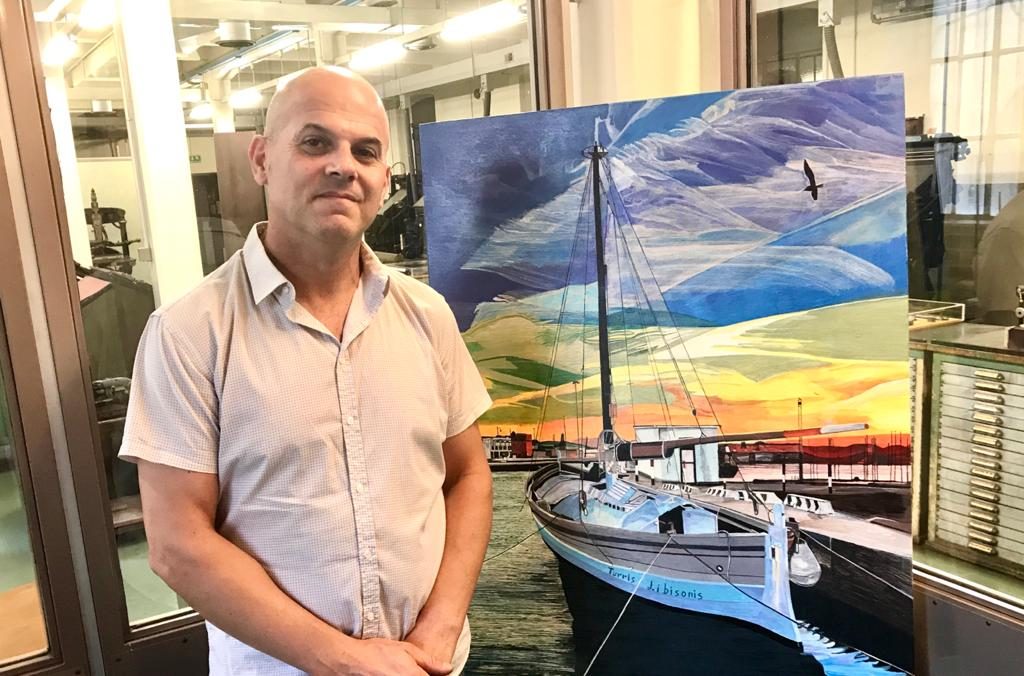 Alex Da Torres accanto a un suo dipinto di una barca al molo, durante un'esposizione